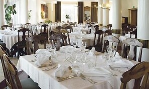A banquet hall with multiple round tables set for dining, each with white tablecloths and silverware.