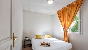 A neatly made bed with a tray of breakfast items, a small bedside table with a plant, and a window with curtains. - Appart’City Classic Dijon – Toison D’or (Ahuy)