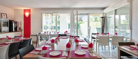 A dining area with tables set for multiple people, chairs, and a counter with a cash register.
