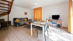 A modern living room with a staircase, a dining area, a TV, and a desk. - Appart’City Classic Dijon – Toison D’or (Ahuy)
