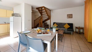 A modern kitchen with a dining area, a staircase, and a living room with a sofa and cushions. - Appart’City Classic Dijon – Toison D’or (Ahuy)