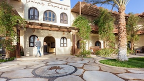 A building with a sign reading "Dahab Paradise," featuring a courtyard with a stone mosaic, palm trees, and arched windows. - Dahab Paradise (Dahab)