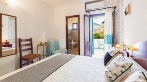 Ein Schlafzimmer mit einem Bett, einem Sessel, einem kleinen Tisch und einem durchgehenden Türbogen einsehbaren Badezimmer.