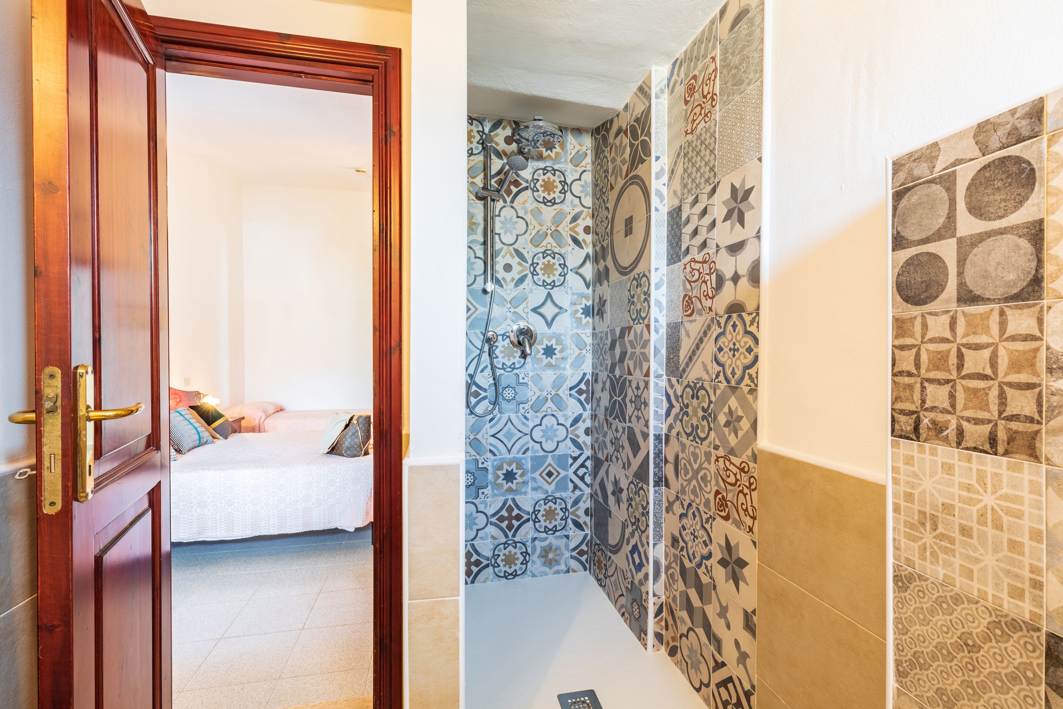 A hotel room with a wooden door, a bed with pillows, and a bathroom with patterned tiles.