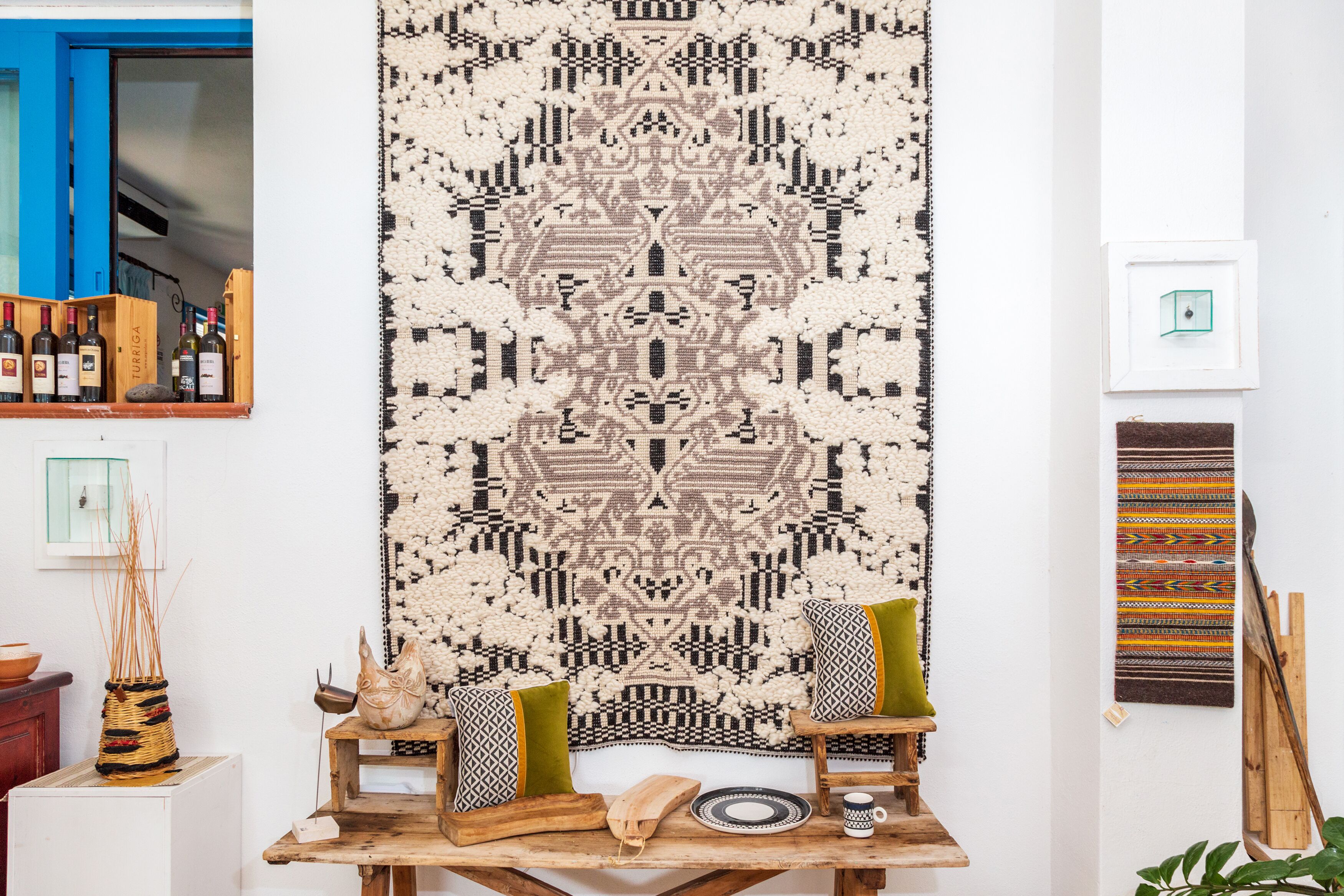A room with a large woven tapestry, a wooden table with a bowl, a vase, and a plate.