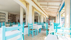 Ein Restaurant mit türkisfarbenen Stühlen und weißen Tischen, Steinböden und einer hohen Decke mit Holzbalken.