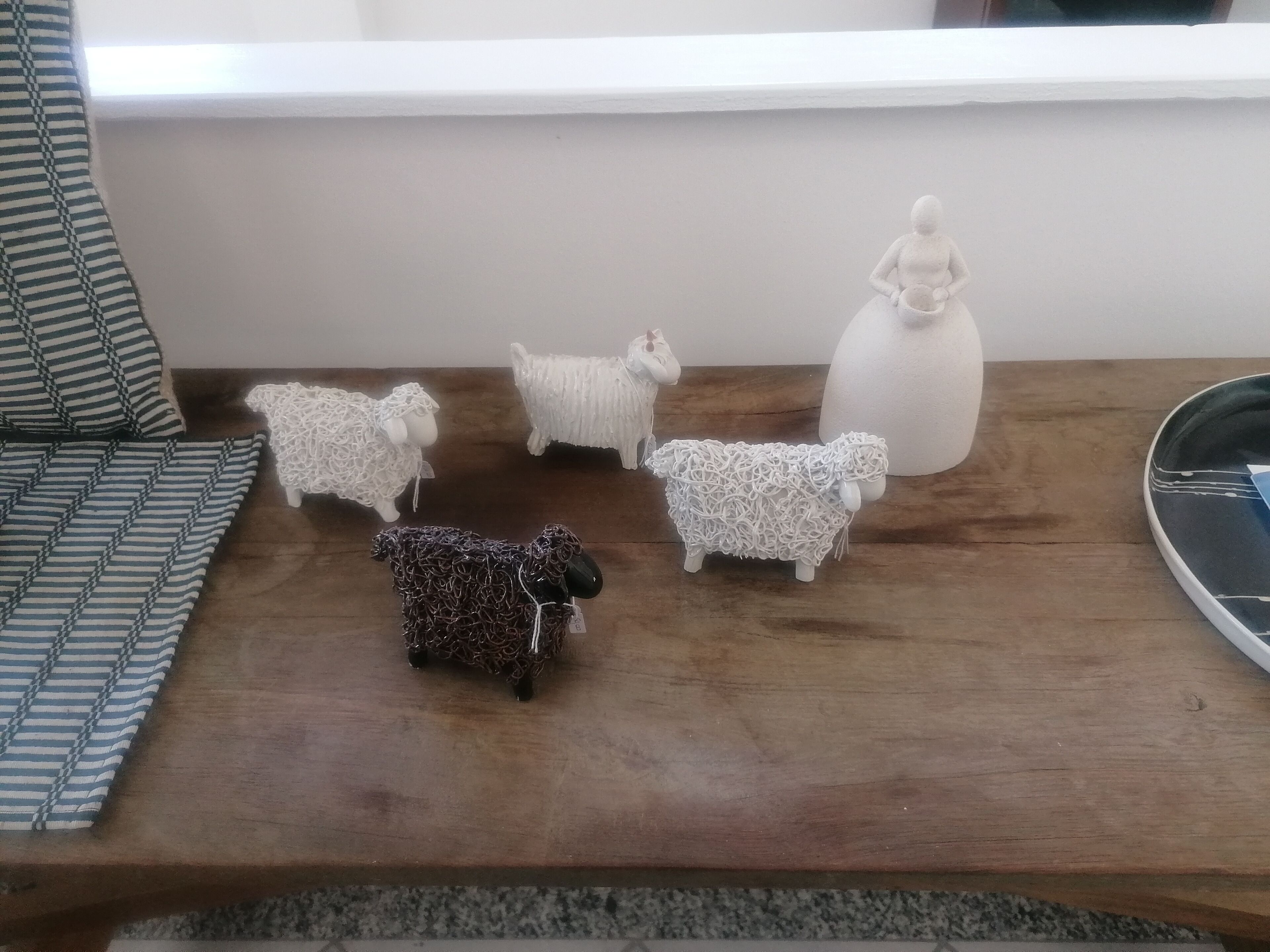 A wooden table with six sheep figurines and a white vase.