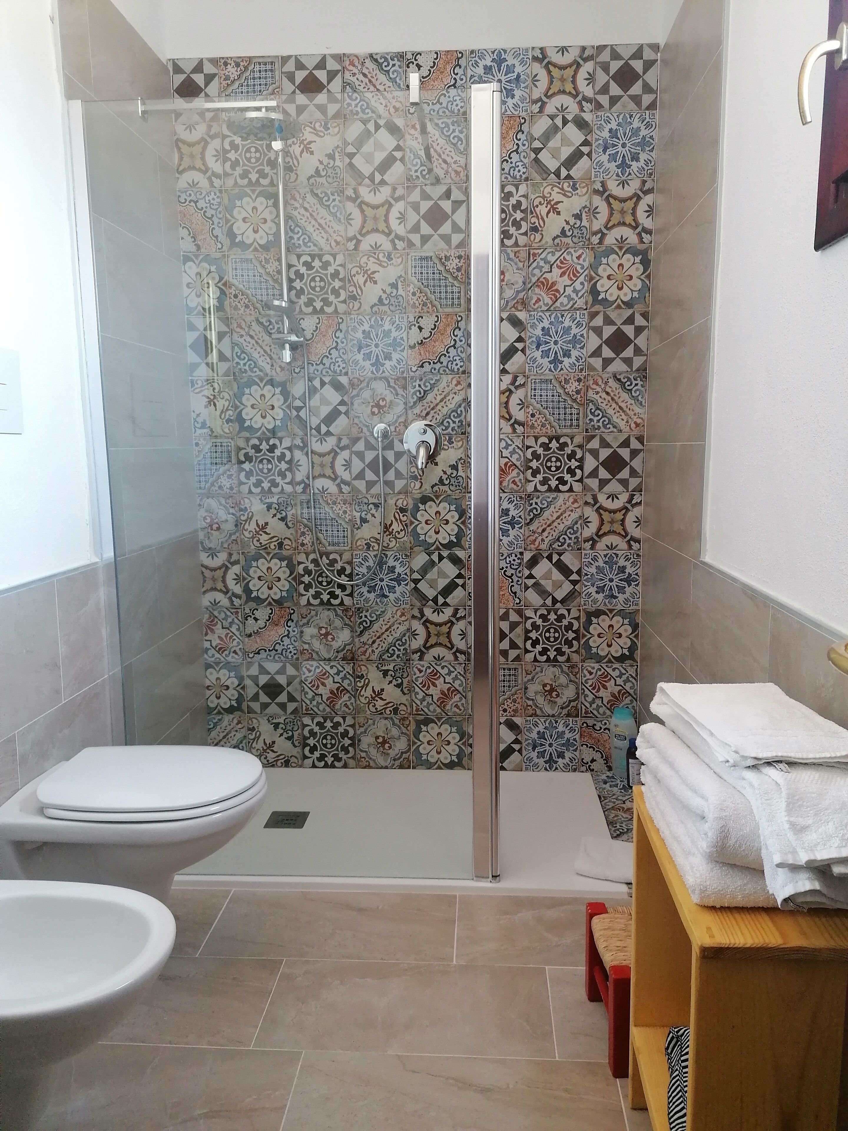 Un bagno con doccia, wc e una pila di asciugamani su uno scaffale in legno.