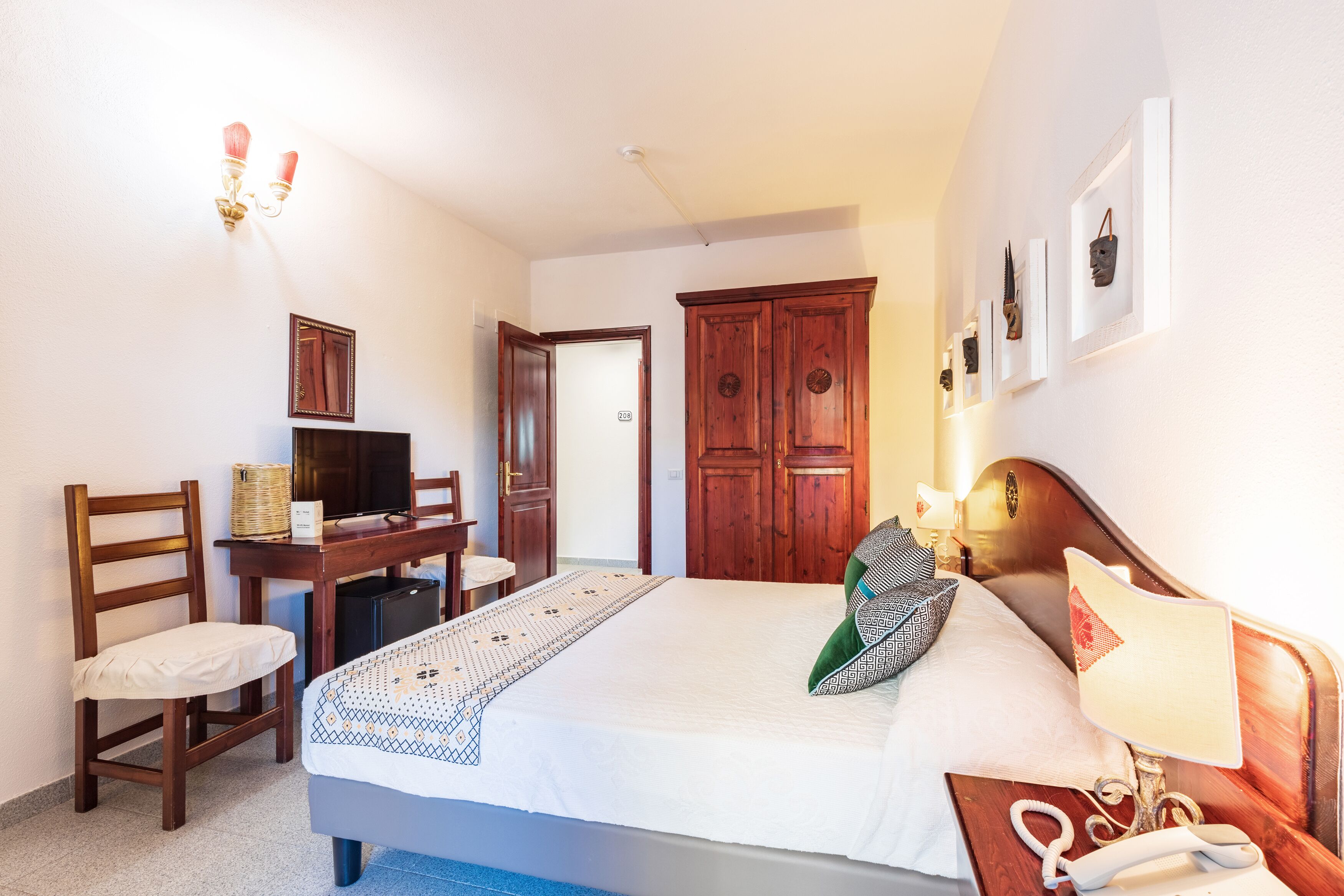 Una camera d'albergo con un letto, una scrivania, una sedia, una televisione e un armadio.