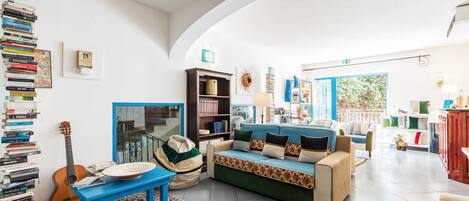 A spacious living room with a green sofa, a blue coffee table, and a bookshelf filled with books.