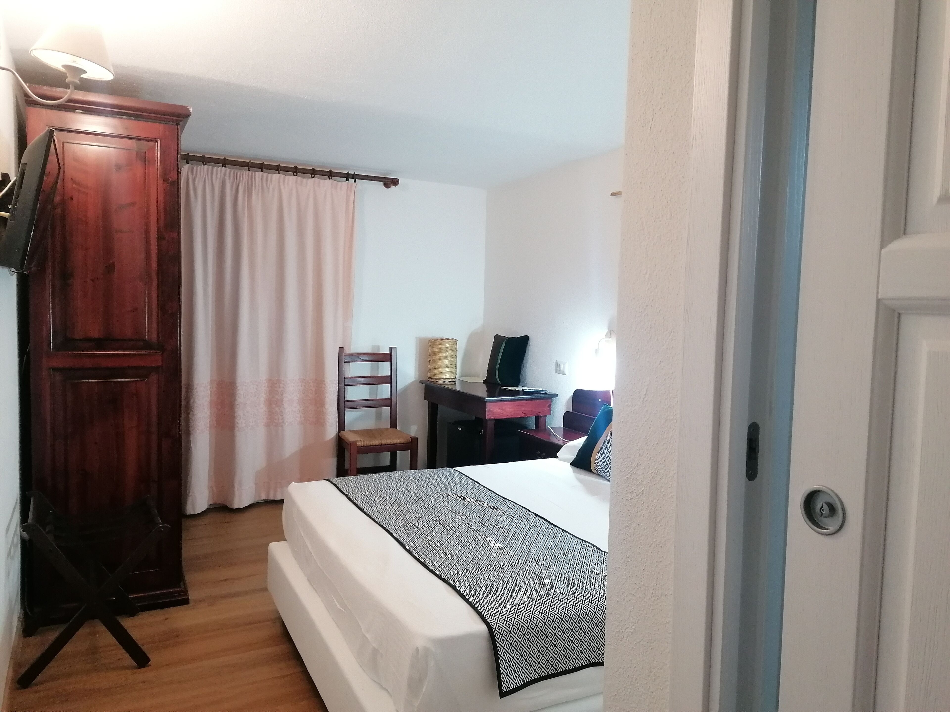 A bedroom with a bed, a desk, a chair, a wardrobe, and a curtain.