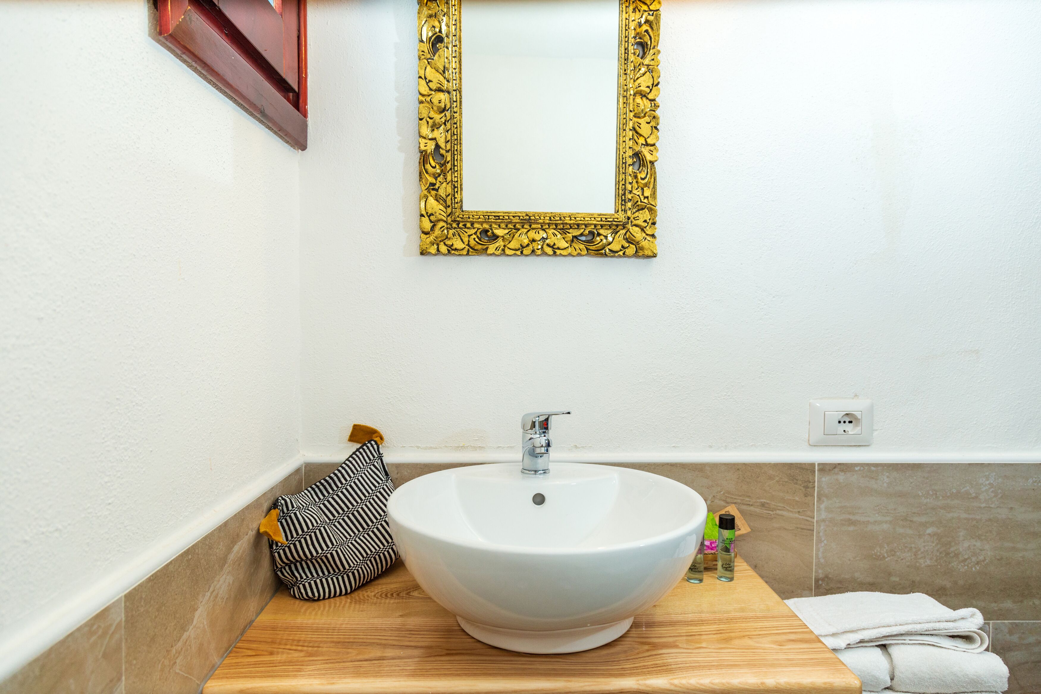 A bathroom with a white sink, a wooden countertop, a gold-framed mirror, and a towel rack.