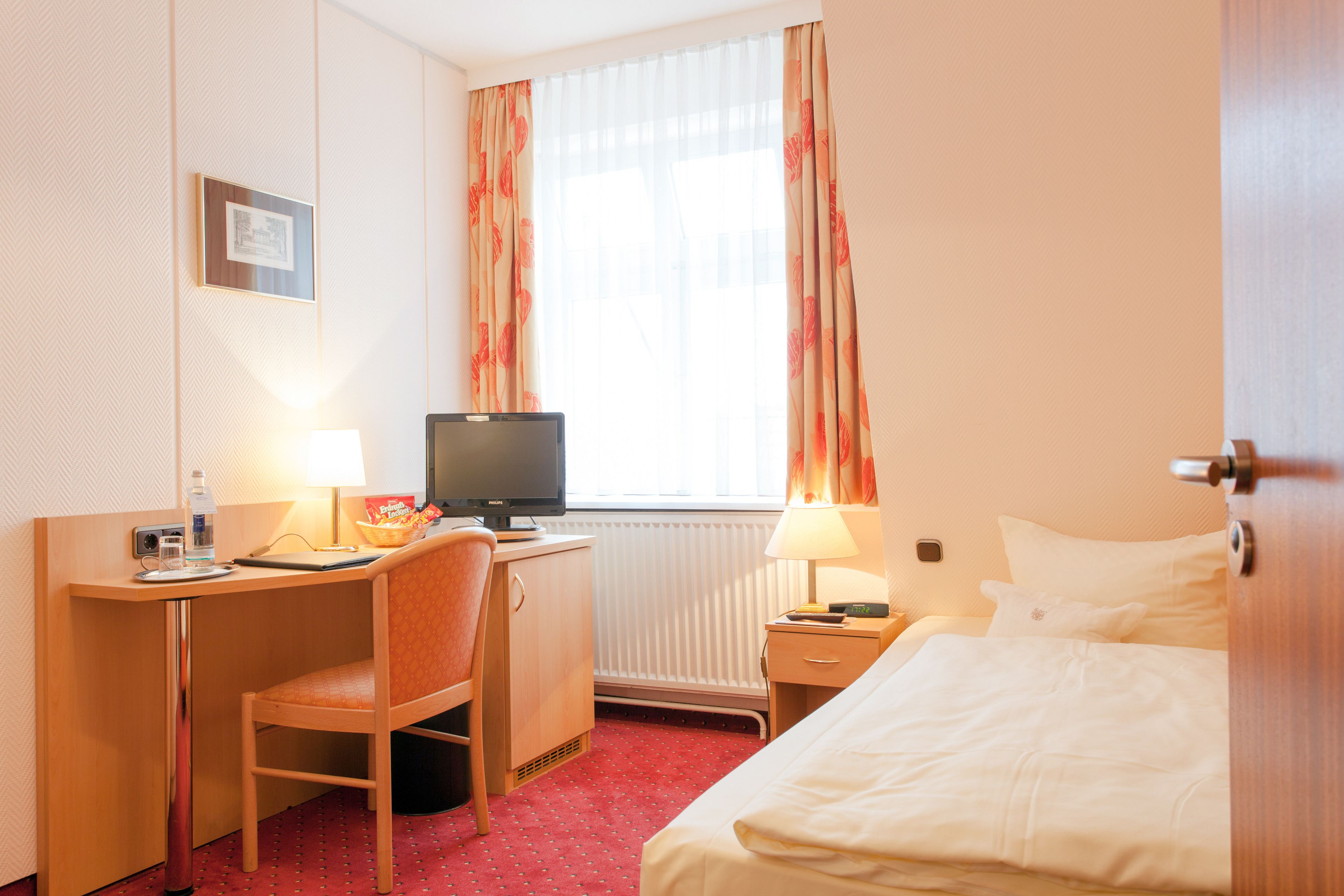 A hotel room with a bed, desk, chair, television, and a window with curtains.