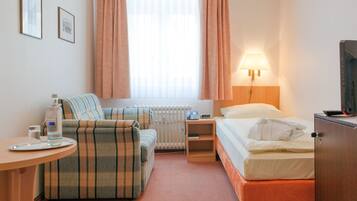 Quarto de hotel com cama, sofá, mesa com um copo de água, luminária e radiador.