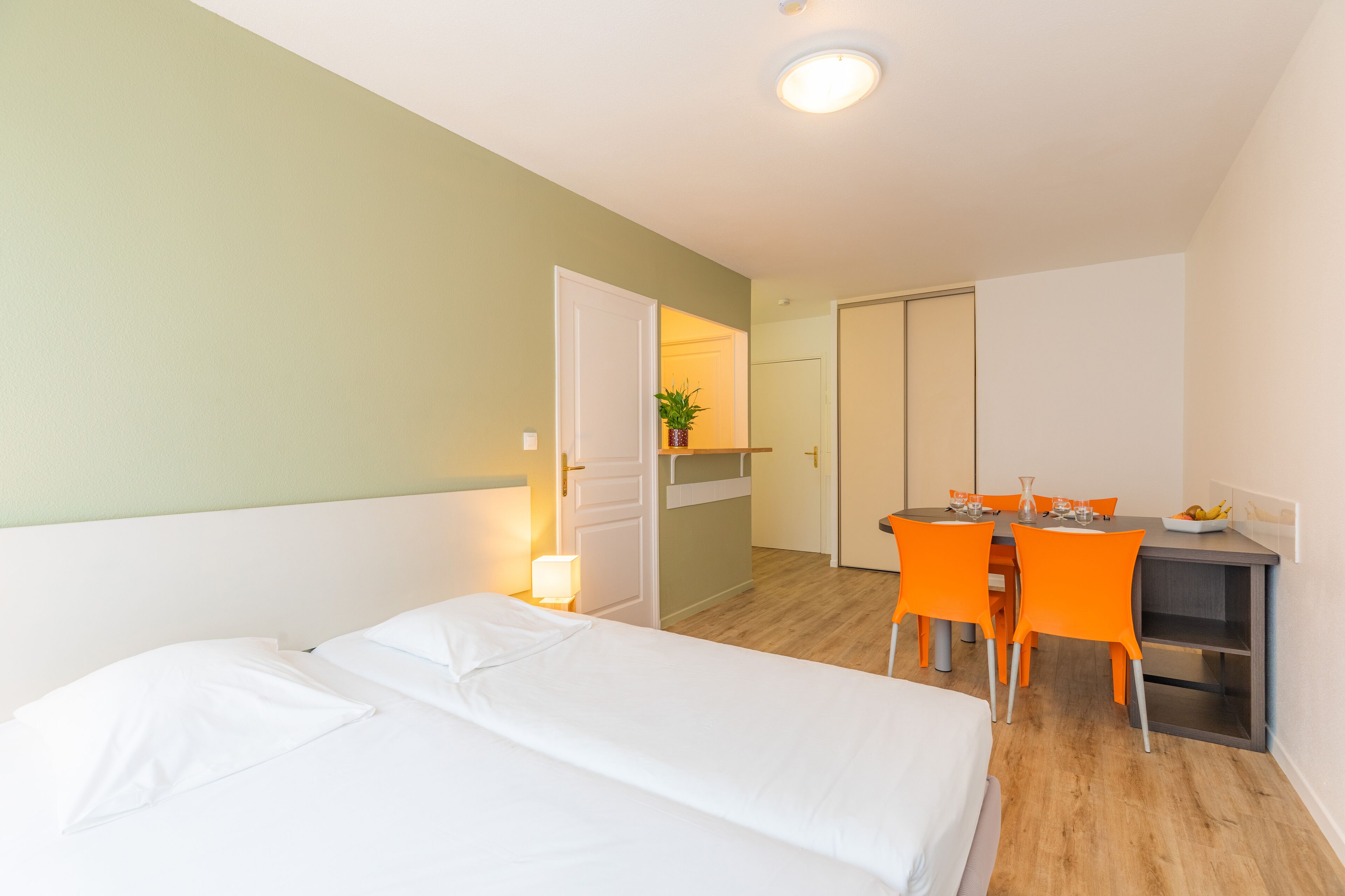 A hotel room with a bed, a desk, and a chair. There is a door leading to another room.