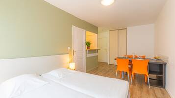 A hotel room with a bed, a desk, and a chair. There is a door leading to another room.