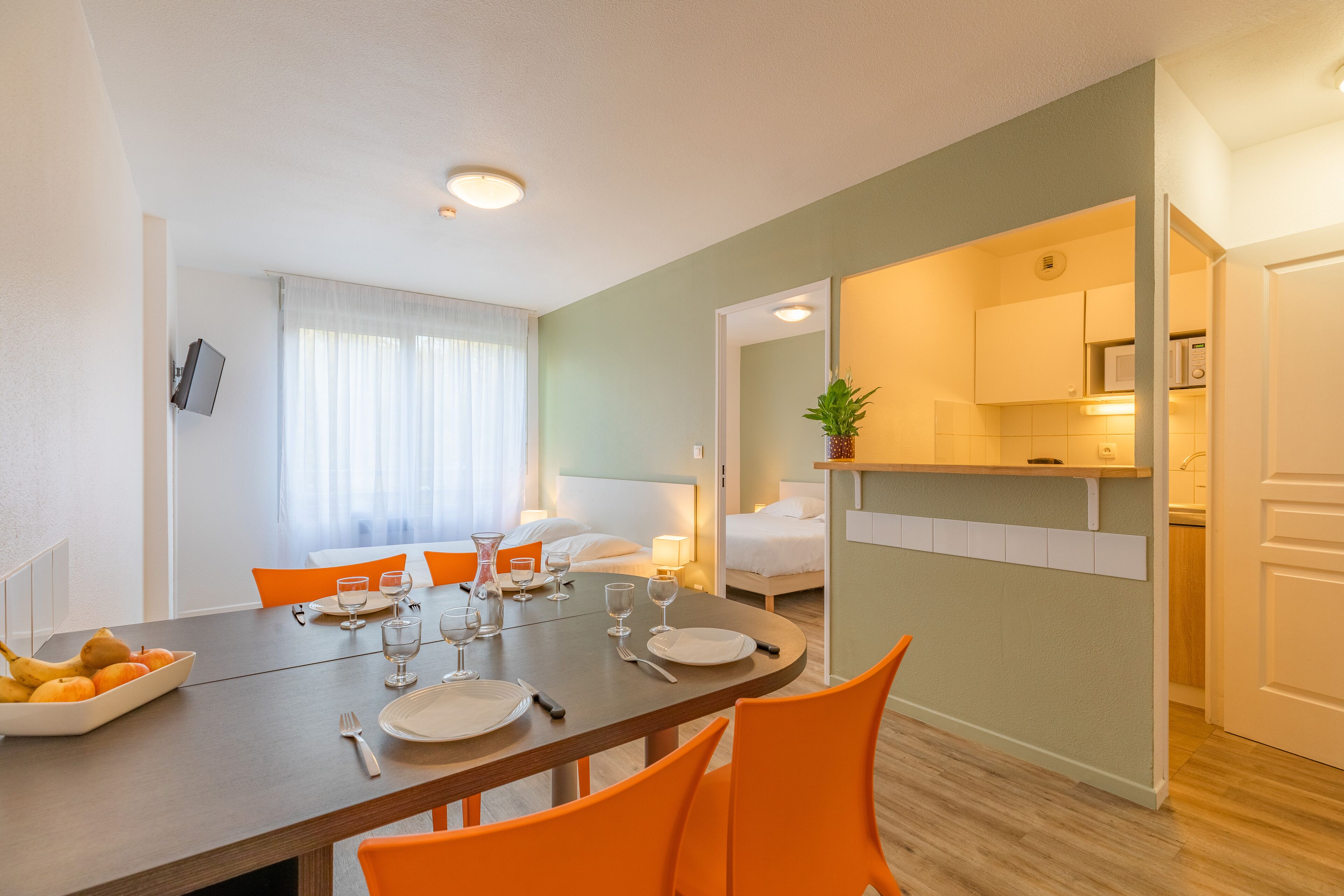 A modern hotel room with a dining area, a kitchen, and a bathroom.