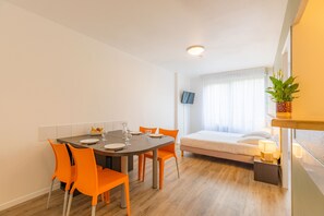 A modern room with a dining table, orange chairs, a bed, a TV, and a potted plant.