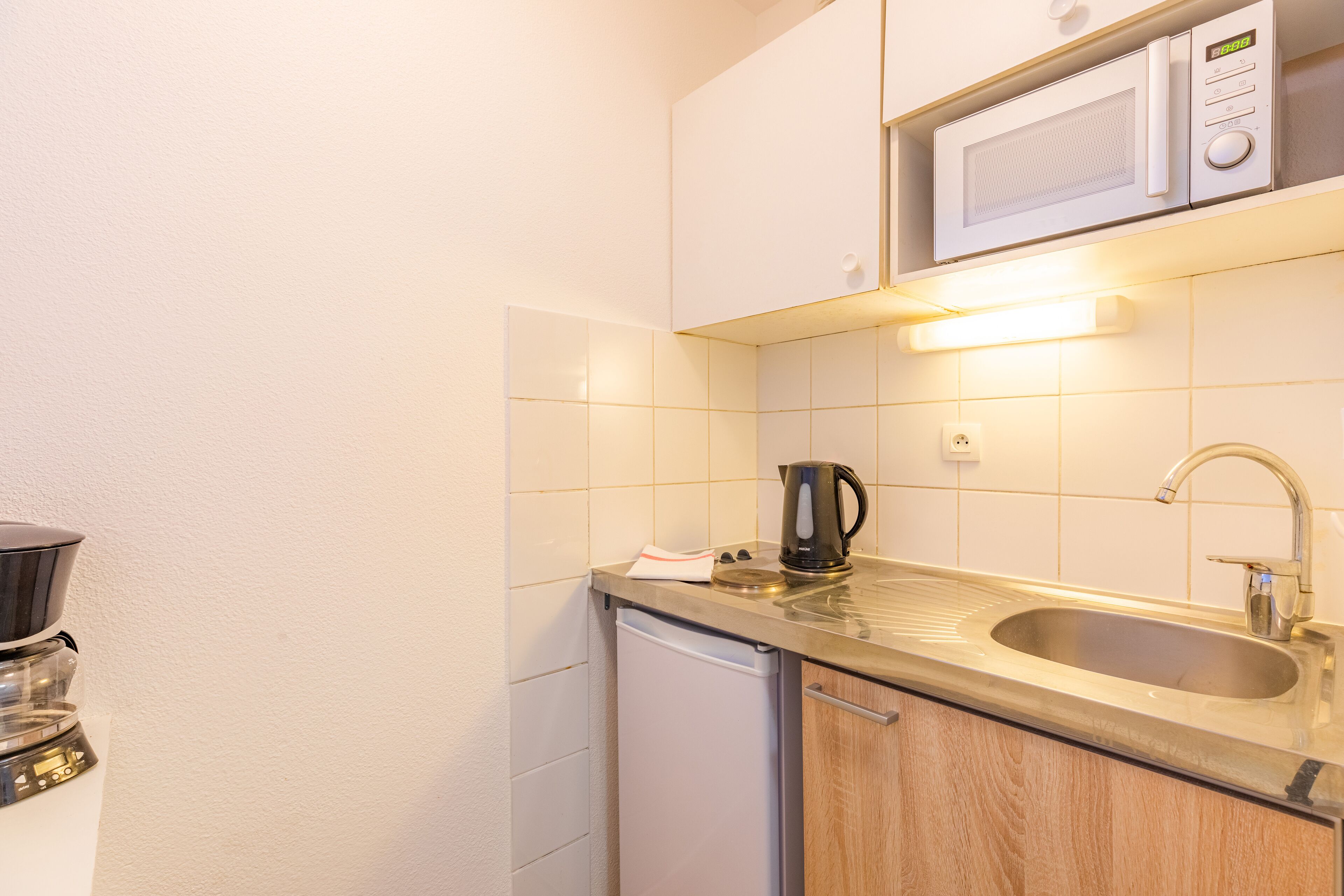 A compact kitchen with a microwave, sink, and coffee maker.