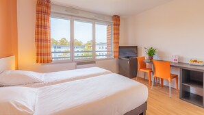 Habitación de hotel con dos camas, un escritorio con televisor y una zona de comedor con sillas anaranjadas.