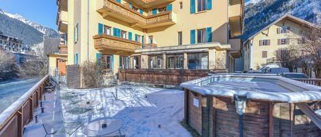 Un hotel de varios pisos con balcones, mobiliario exterior y un patio cubierto de nieve.