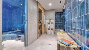 Un baño moderno con cabina de ducha de vidrio, puerta de madera y una pequeña mesa con un libro y una taza.