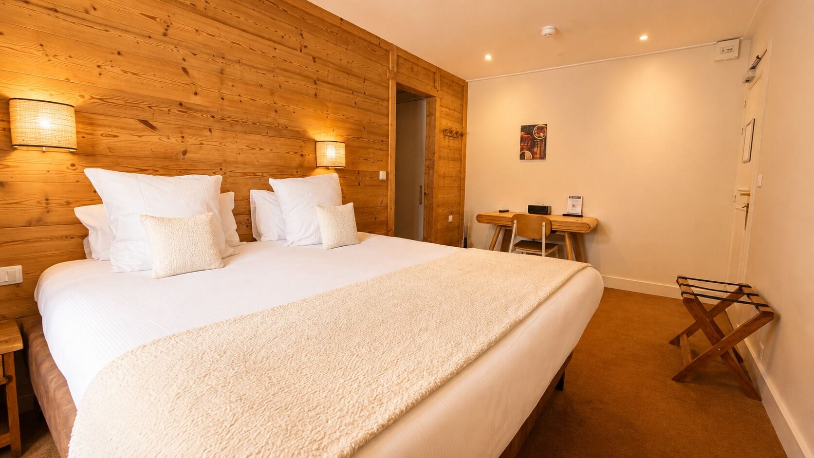 Habitación de hotel con una cama grande, paredes de paneles de madera, un escritorio y una silla.