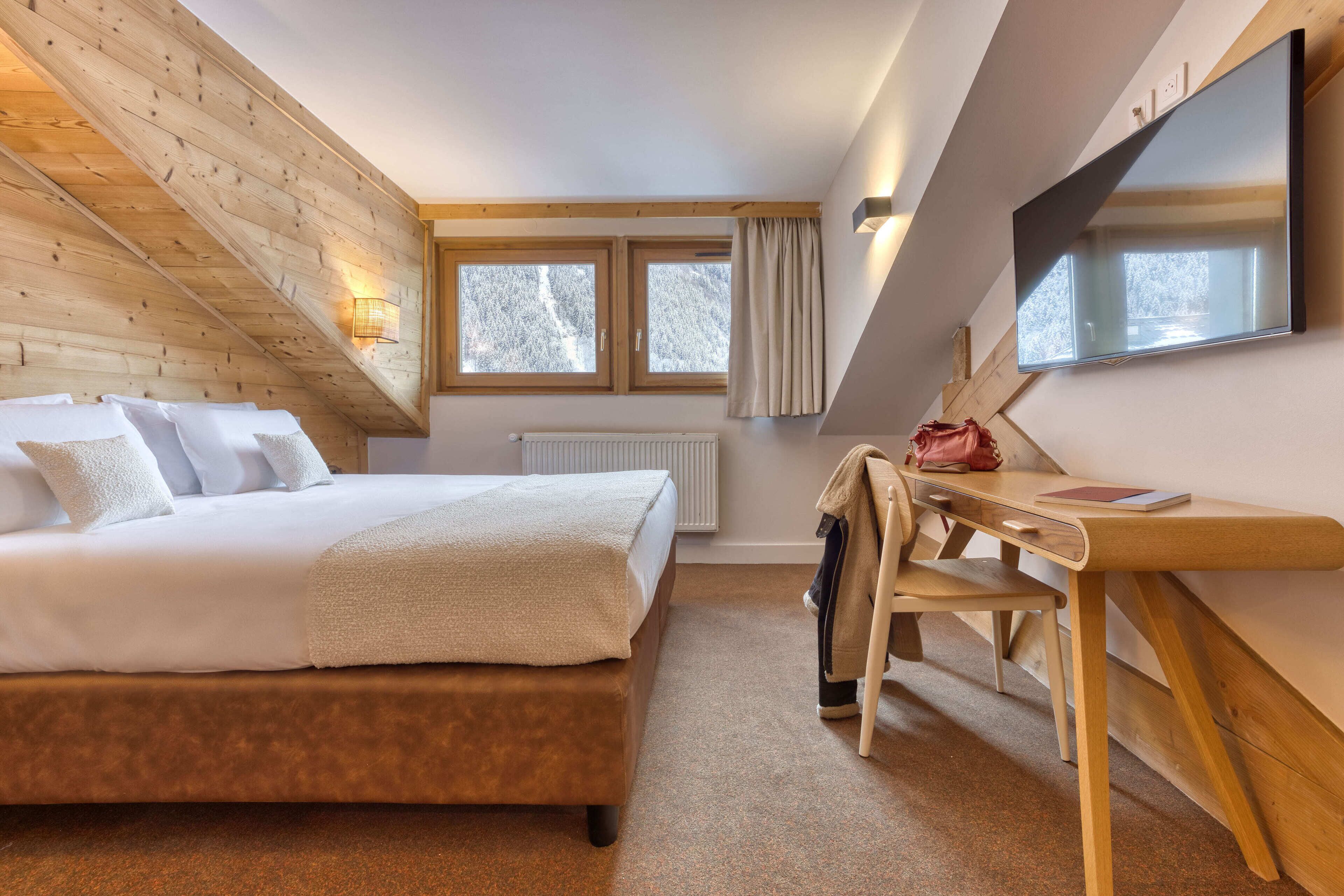 A bedroom with a bed, a desk, and a TV.