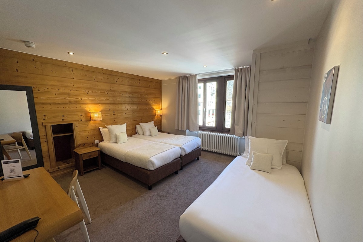 Une chambre d’hôtel avec deux lits, un mur en bois, un bureau et une fenêtre avec des rideaux.