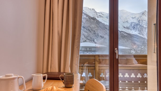 Una habitación acogedora con una mesa de madera, un croissant, un paño rojo y vistas a montañas nevadas.