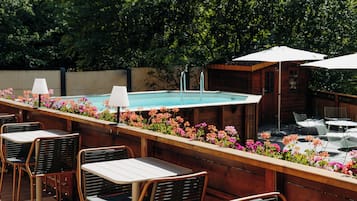 An outdoor pool area with wooden deck seating, a hot tub, and umbrellas.