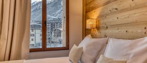 A hotel room with a wooden headboard, a bed with white linens, and a view of snow-covered mountains through a window.