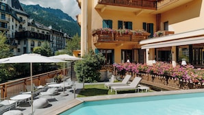 Un hotel con piscina, mobiliario exterior y jardineras en los balcones.