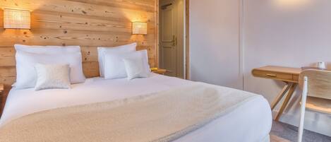 Una cama bien tendida con sábanas y almohadas blancas, un cabecero de madera y dos lámparas fijadas a la pared.