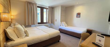 Habitación de hotel con una cama grande, una cama más pequeña, un escritorio con silla y una ventana con cortinas.