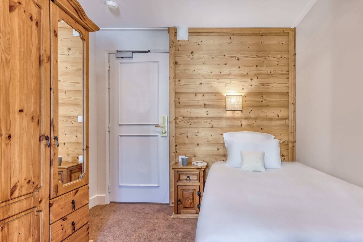 Une chambre à coucher avec une tête de lit en bois, un lit recouvert de draps blancs, une table de chevet avec une lampe et une armoire en bois.