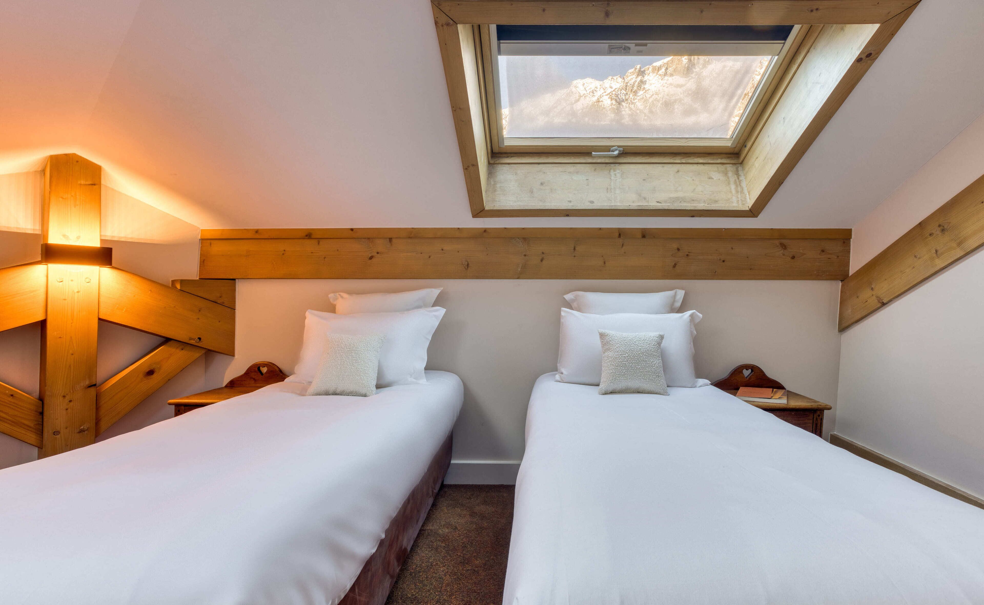 A bedroom with two beds, a skylight, wooden beams, and a nightstand with a book.