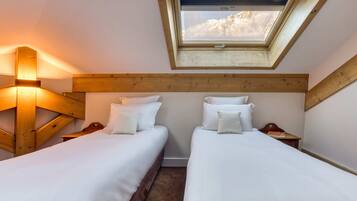 A bedroom with two beds, a skylight, wooden beams, and a nightstand with a book.