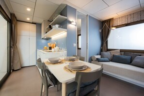 A compact living space with a dining table set for four, a sofa with cushions, and a kitchenette area. - Torre del Porticciolo Camping Village Glamping (Alghero)