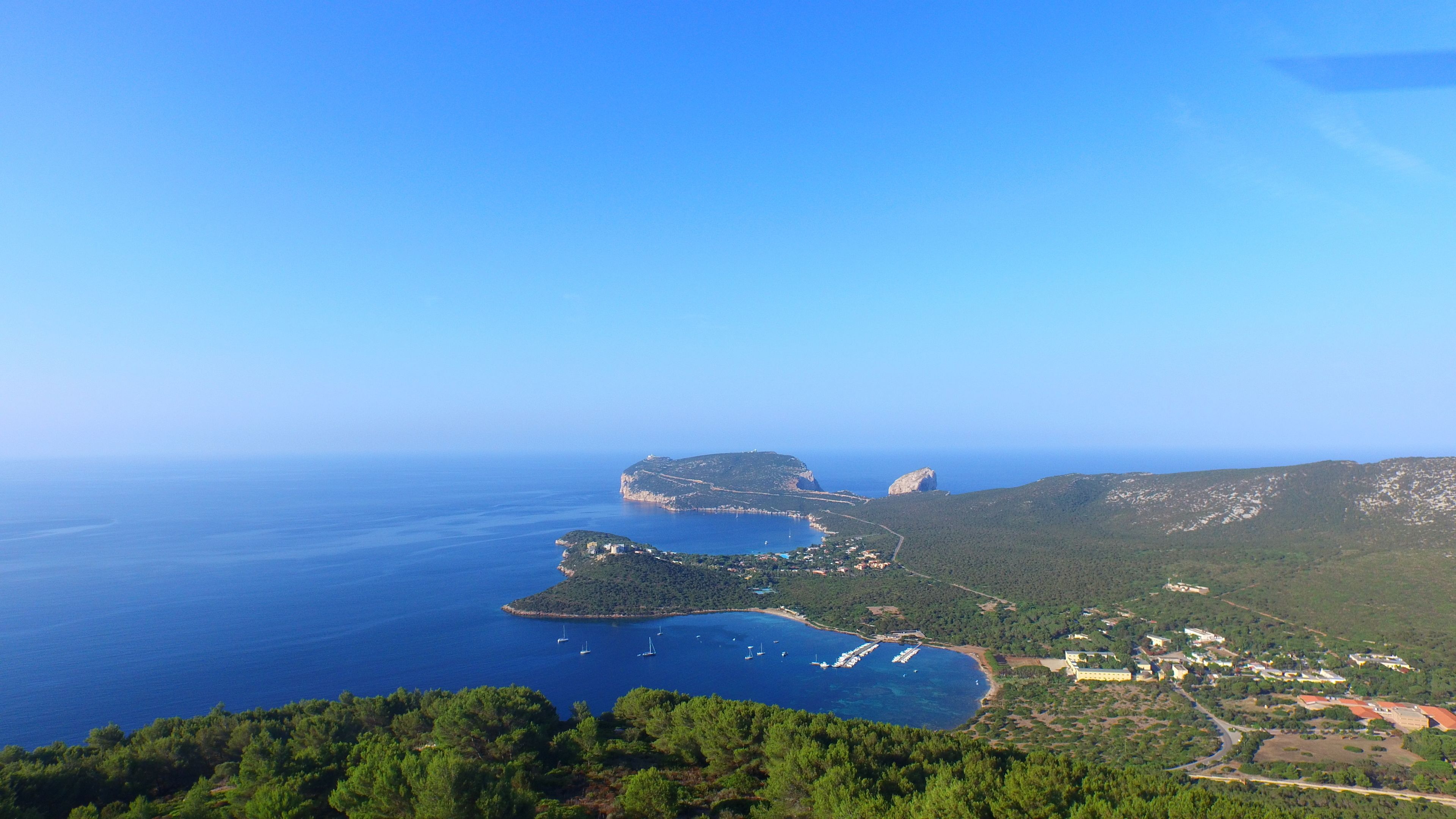 An aerial view of a coastal area with a large bay, a small island, and a town with buildings and roads.