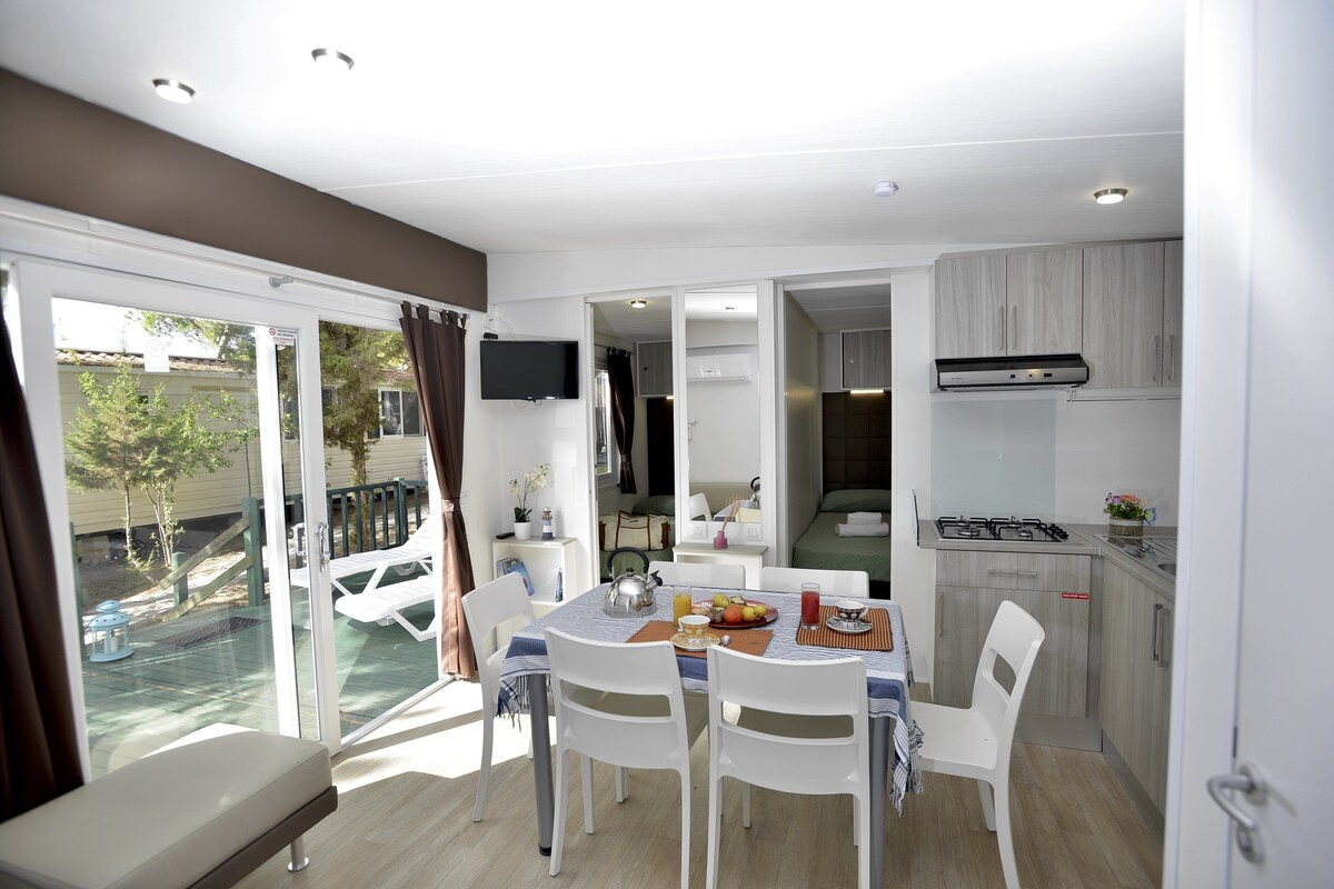 A modern, well-lit room with a dining area, kitchenette, and a sliding glass door leading to an outdoor space.