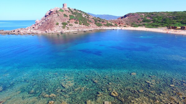 A coastal landscape with clear blue waters, rocky terrain, and a historic tower on a hill. - Torre del Porticciolo Camping Village Glamping (Alghero)