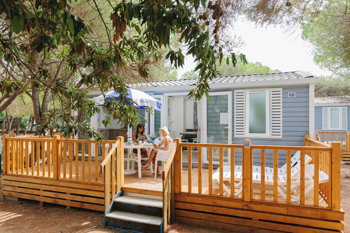 A wooden deck with a railing, a table, and chairs. There is a building with a number 68 on it.