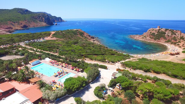 Un resort con piscina, playa y montañas al fondo.