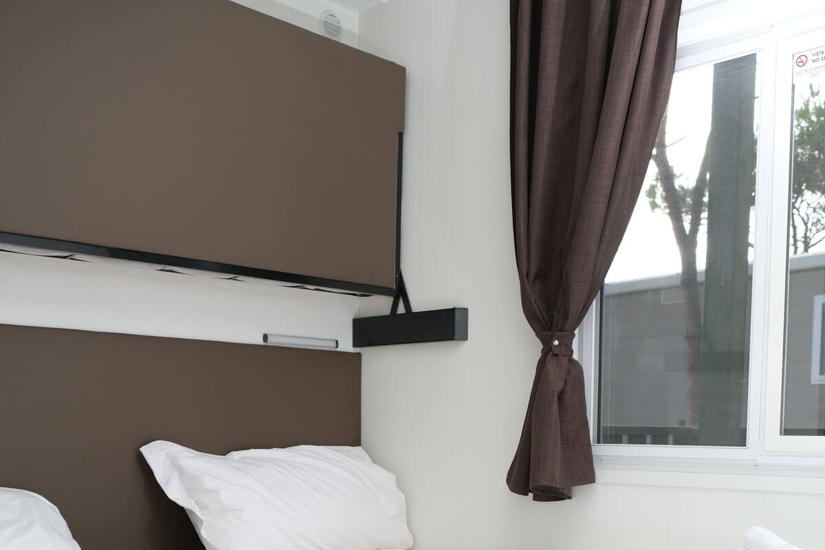Habitación de hotel con dos camas, ropa de cama blanca, cabecero marrón y una ventana con cortinas.