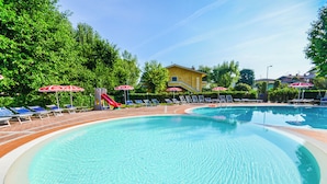 A swimming pool with sun loungers and umbrellas, surrounded by greenery and a building.