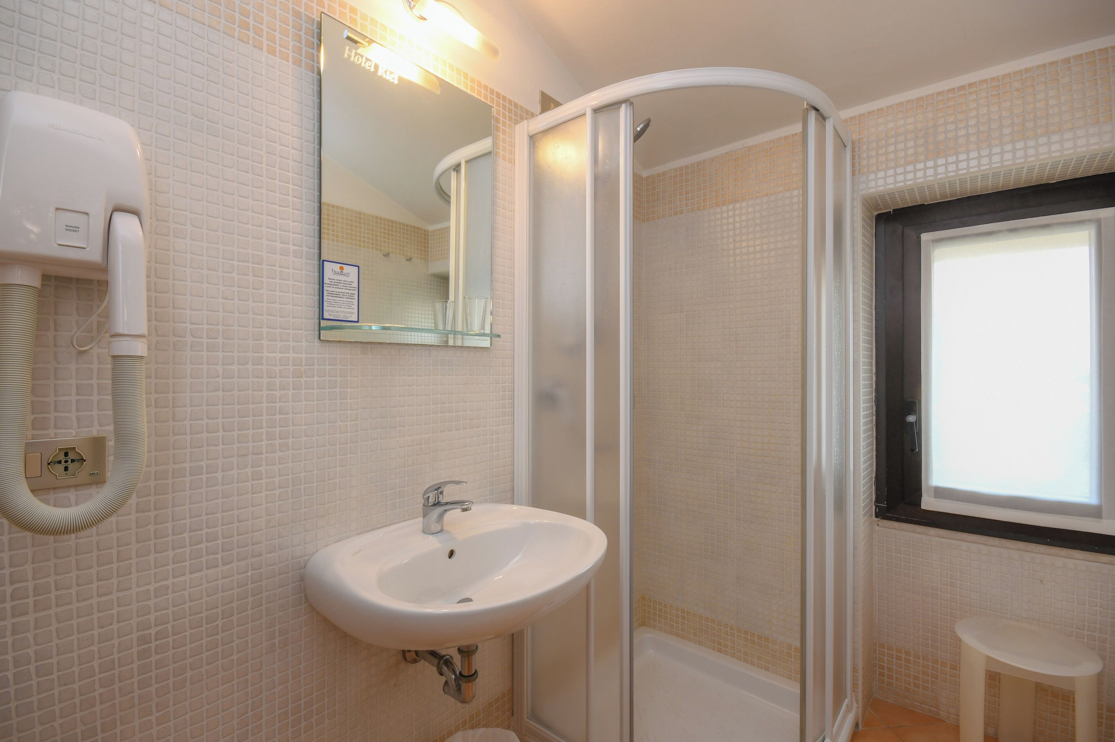 A bathroom with a white sink, a mirror, a shower enclosure, and a window.