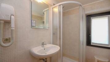 A bathroom with a white sink, a mirror, a shower enclosure, and a window.