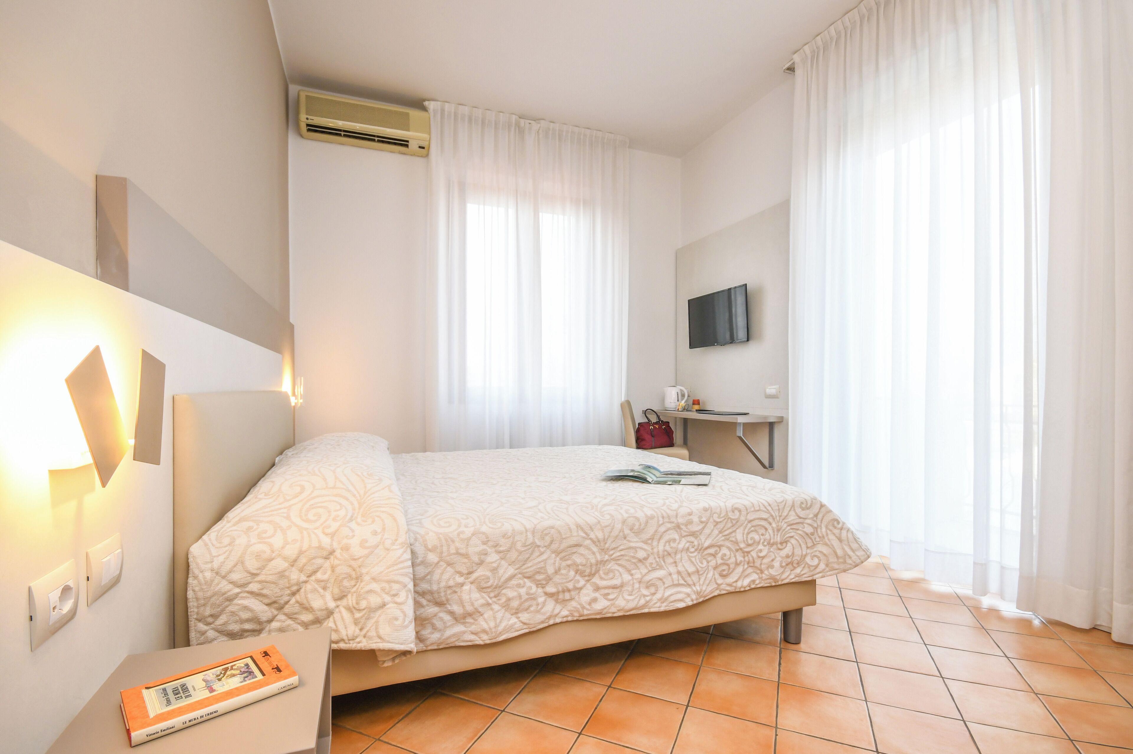 A hotel room with a bed, a desk, a television, and a window with curtains.