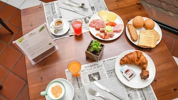 Una mesa de desayuno con un menú, una taza de café, un vaso de jugo de naranja, un croissant, pan y un plato con diversas comidas.